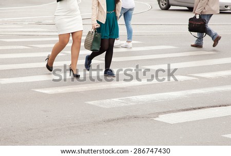 women\'s legs in white skirt and green dress on a pedestrian crossing