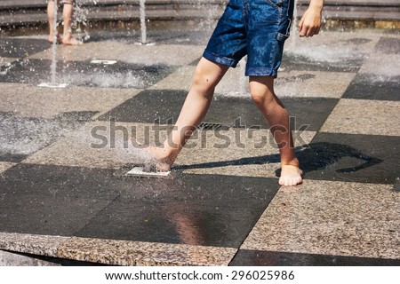 feet of boy in blue jeans playing in the fountain on sunny summer day