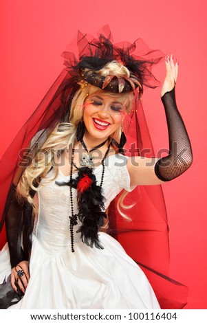 laughing bride wearing black net gloves and unusual hat with veil on red background