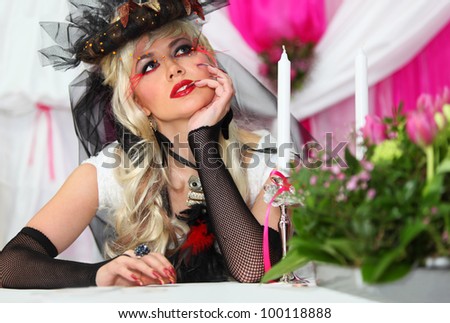 beautiful bride wearing black net gloves and unusual hat sits at table with candles and dreams