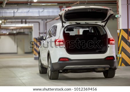 Modern white car with open trunk door at underground parking.