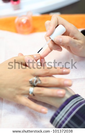 Female hands manicure woman by transparent nail polish in beauty salon