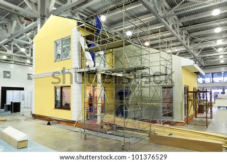 Team of builders build two-storey yellow cottage in large hall