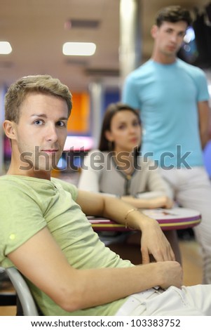 Young man sits at table; other man stands and woman sits at table; focus on left man; shallow depth of field