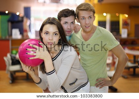 Woman prepares to throw of pink ball in bowling; two men look at aim; focus on woman; shallow depth of field