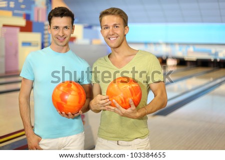 Two young happy men hold orange balls in bowling club; shallow depth of field