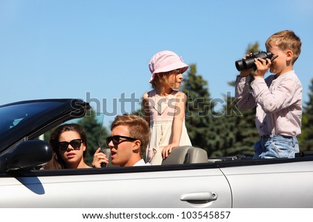 Happy father, mother and two children ride in convertible car and play; focus on man