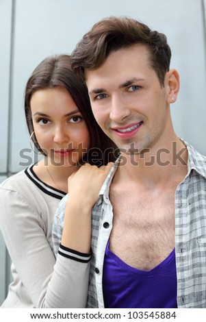 Beautiful smiling man and woman stand near gray wall; woman holds man shoulder; focus on man