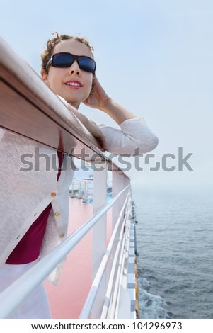 Beautiful woman wearing sunglasses stands on board of ship an looks into distance