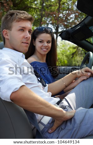 Young girl and a guy sit in the car and hold hand each other, the girl on the driver seat, the focus is on the face of a guy