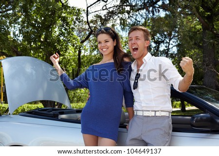 Young girl and her boyfriend stand leaning at car and show triumph gesture with their hands, boy shouts