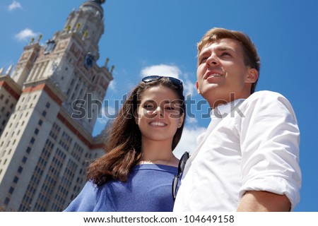 Young smiling couple stands on the background of blue sky near to Lomonosov Moscow State University .