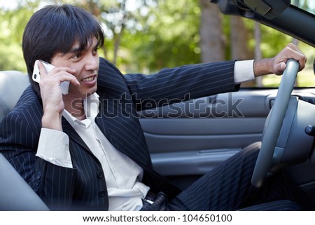 Man in a striped suit sits on a driver seat in a open top car and talk on a cell phone