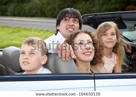 Family of four - parents and son with daughter -  sits in a cabriolet and looks on the sky.