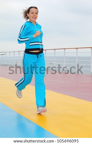 Happy woman wearing in blue sports suit runs on cruise liner deck
