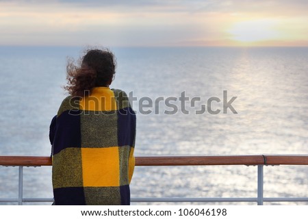 Back of woman wrapped in plaid standing on cruise liner deck and look at horizon