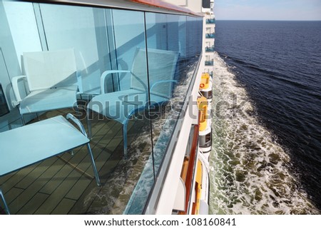 glassy balcony with white chairs and table on cruise liner; ship board and deep blue sea with foam