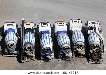 Six concrete mixer machines stand on asphalt at sunny day; back view