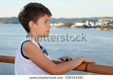 Thoughtful boy stands on board of ship and looks at beautiful landscape