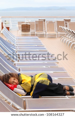 Woman wearing in red mittens and plaid sleeps on lounger at ship deck