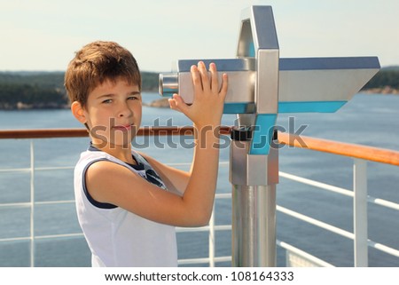 Boy stands on board of ship near big binoculars and looks at camera