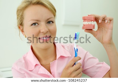 Dentist shows how to correctly brush teeth and looks at camera in dental clinic.