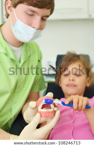 Dentist shows to patient girl how to correctly brush teeth. For clarity, doctor uses an artificial jaw. Focus on jaw.