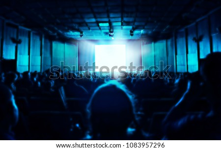 silhouette of people sitting in dark cinema hall, blue glow from screen, blurred background