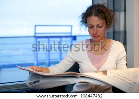 Young girl read newspaper in cabin of big passenger ship with view on sea