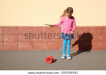 Beautiful little girl plays with yo-yo on sunny day outdoor.