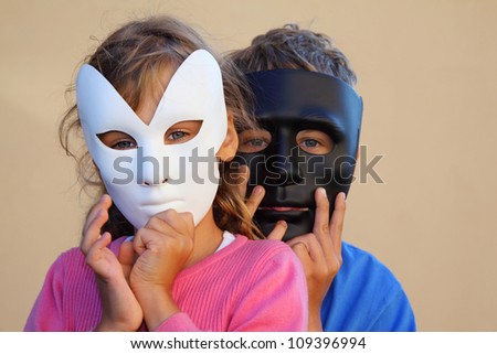 Girl and boy hide faces behind black and white masks. Focus on girl.