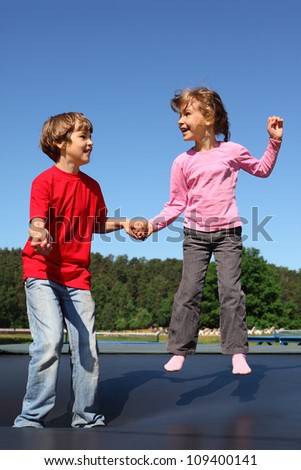 Happy brother and sister jump on trampoline on sunny summer day