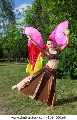 Woman wearing beautiful dress dances with pink veil fans in countryside.