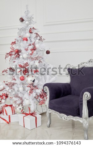 Decorated Christmas tree, gift boxes and armchair with violet upholstery in white room.