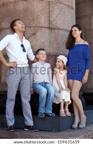 Two kids sit on base of granite column and young man and girl stand on sides, he laughs out loud