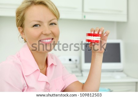 Smiling young dentist keeps toy jaw in cabinet of dental clinic.