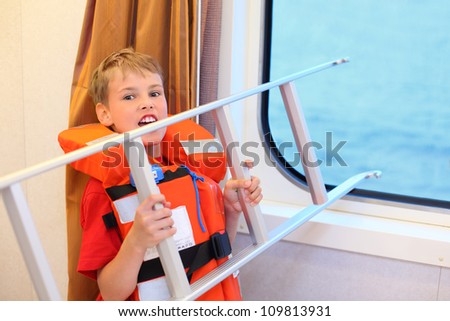 Boy dressed in life jacket screams and holds ladder in cabin of ship