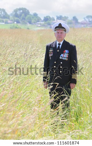 Grandfather in form, cap, ordens, medals stand attention  in field near wood