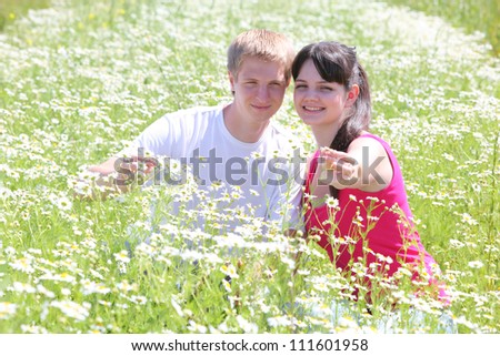 young couple seat in camomile field, girl hold flower in hand