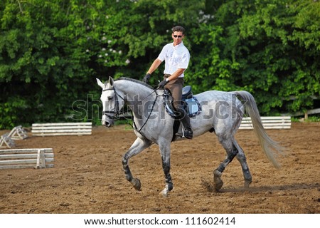 Jockey in glasses rides horse near barrier on hippodrome