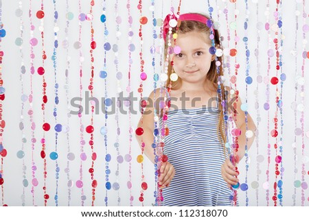 Little girl in striped sundress looks out from behind curtain of plastic beads.