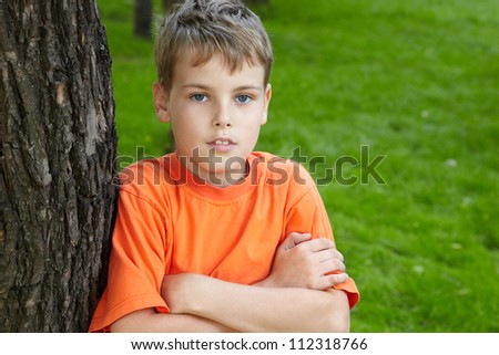 Portrait of boy in orange t-shirt, standing with folded arms in park