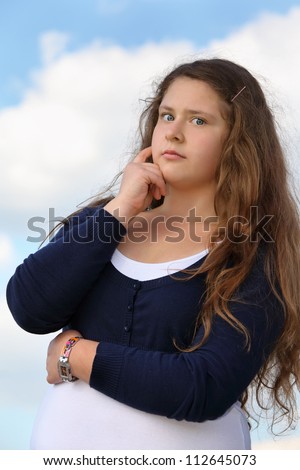Beautiful surprised girl looks at camera at background of blue sky with clouds.