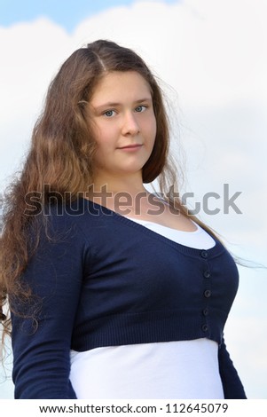 Beautiful fat girl looks at camera at background of blue sky with clouds.