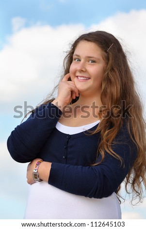 Beautiful smiling girl looks at camera at background of blue sky with clouds.