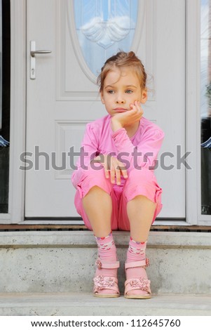 Little sorrowful girl sits on stairs near white door and thinks.
