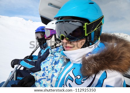 Three skiers in special clothing and helmets ride on cable car in mountains.