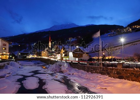 River covered by ice and several hotels in mountains at winter night.