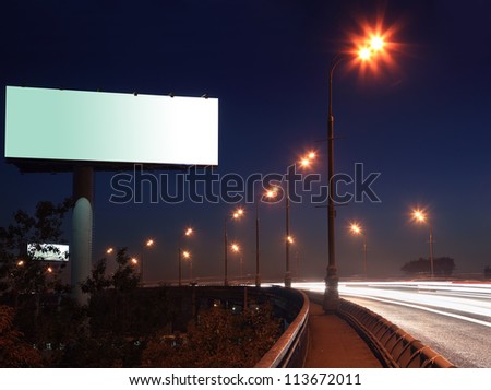 Road with lights and large blank billboard at dark night in city.