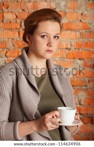 brown-haired woman hold cup, plate near brick wall, half body